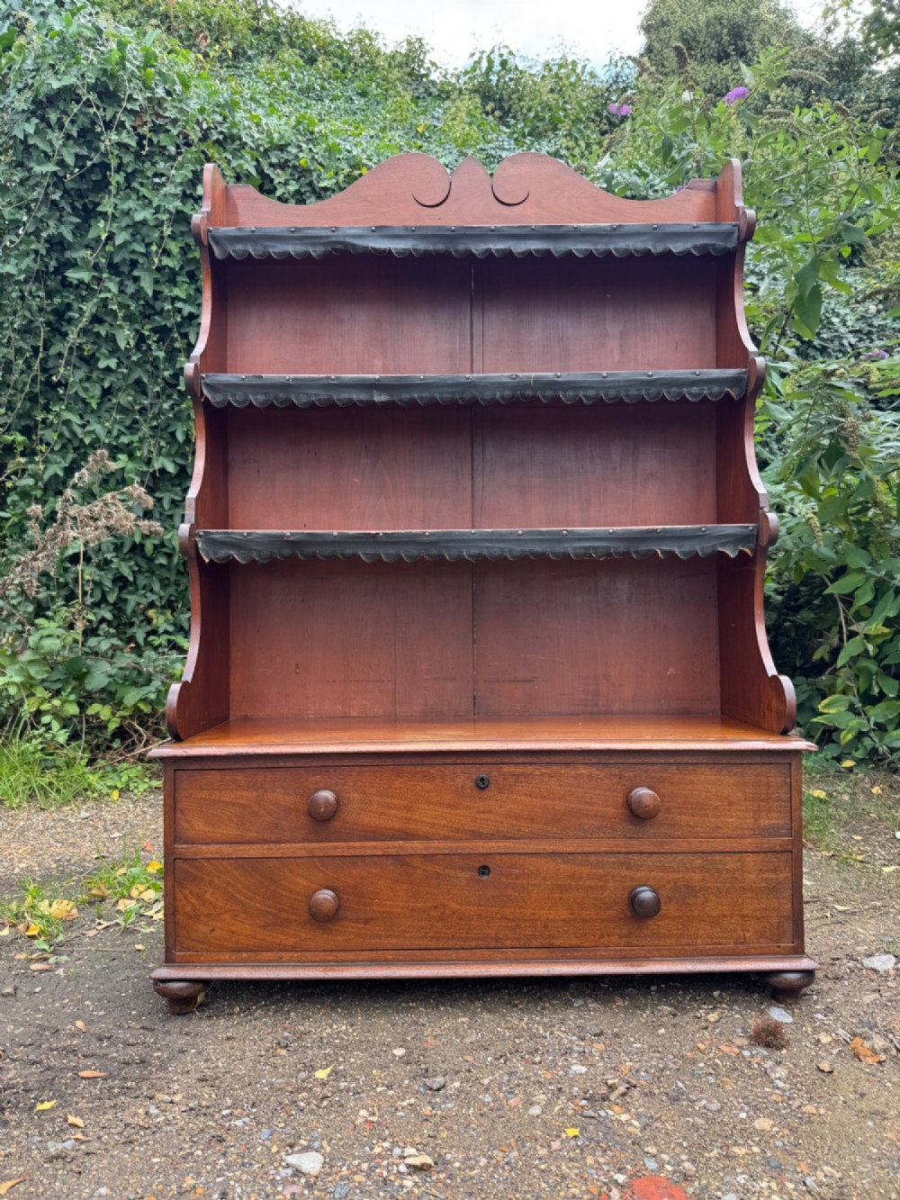 An antique mahogany waterfall bookcase featuring four open graduated shelves with dark trim above two lower drawers with turned wood knobs. View II