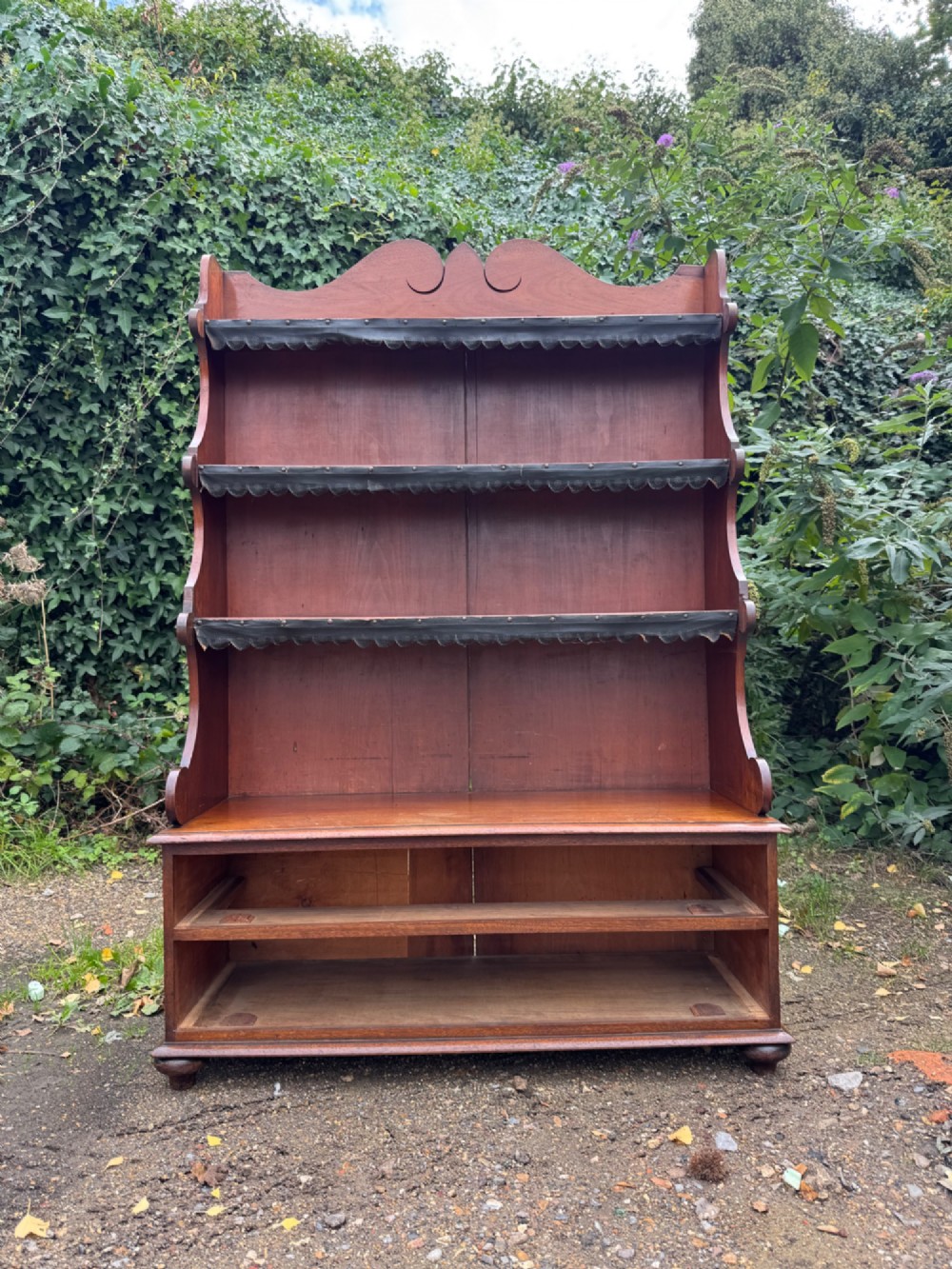 An antique mahogany waterfall bookcase featuring four open graduated shelves with dark trim above two lower drawers with turned wood knobs. View III