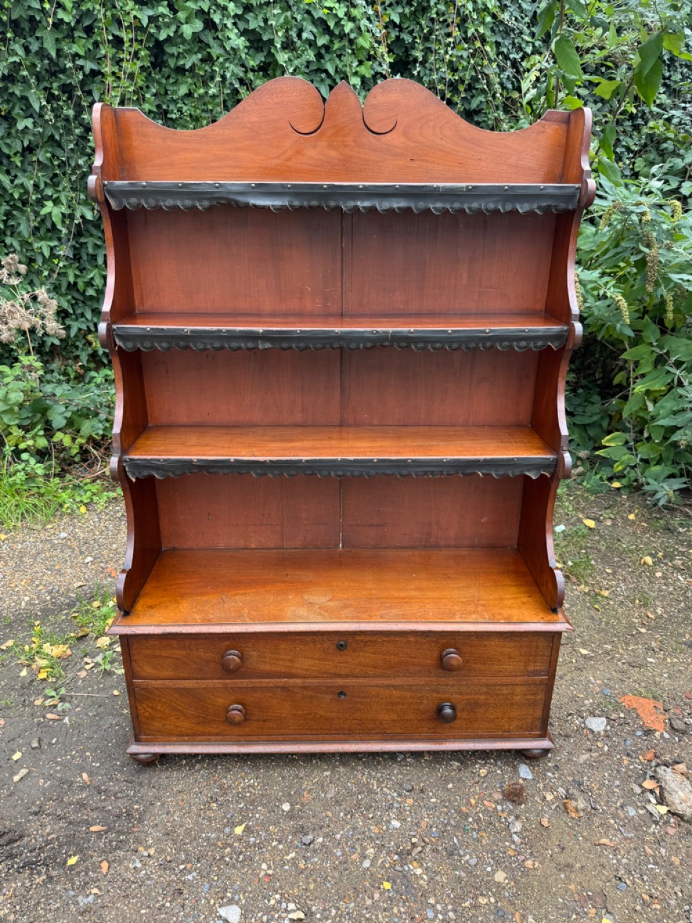 An antique mahogany waterfall bookcase featuring four open graduated shelves with dark trim above two lower drawers with turned wood knobs. View IV