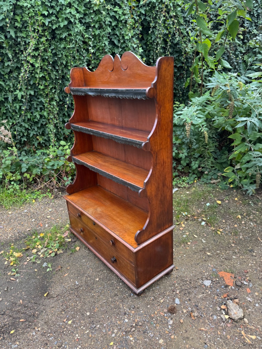 An antique mahogany waterfall bookcase featuring four open graduated shelves with dark trim above two lower drawers with turned wood knobs. View V