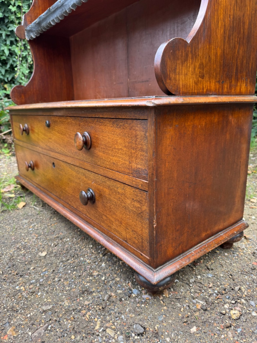 An antique mahogany waterfall bookcase featuring four open graduated shelves with dark trim above two lower drawers with turned wood knobs. View VI