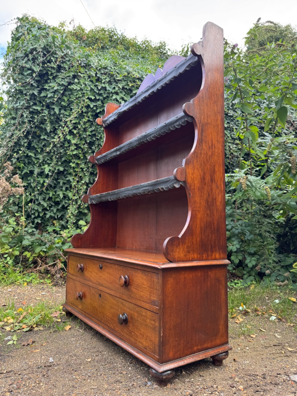 An antique mahogany waterfall bookcase featuring four open graduated shelves with dark trim above two lower drawers with turned wood knobs. View VII