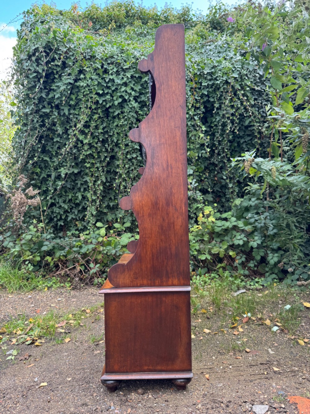 An antique mahogany waterfall bookcase featuring four open graduated shelves with dark trim above two lower drawers with turned wood knobs. View XII