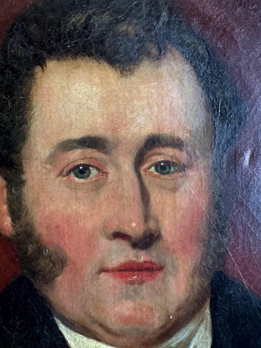 An antique oil painting depicting a gentleman in a dark coat and white neckcloth seated before a red drape, housed in a moulded giltwood frame. View IV