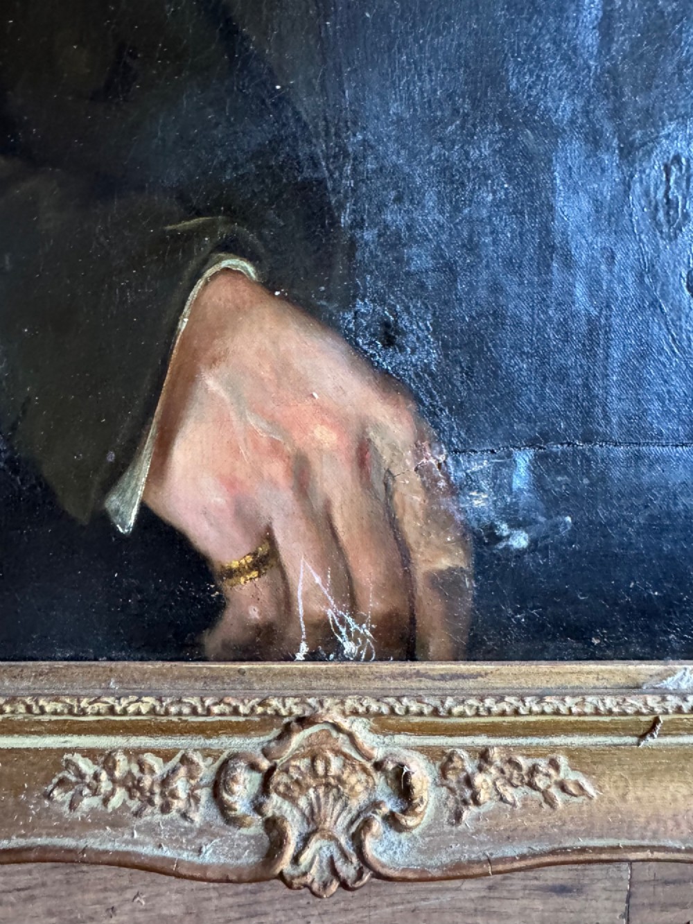 An antique oil painting depicting a gentleman in a dark coat and white neckcloth seated before a red drape, housed in a moulded giltwood frame. View V