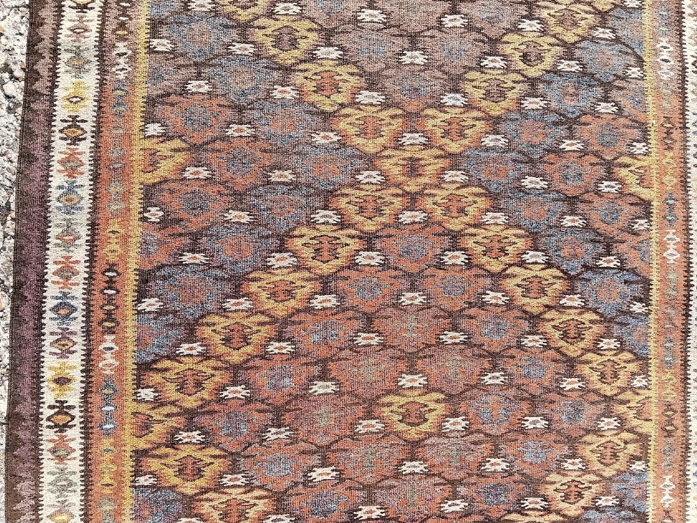 A long handwoven wool kilim runner rug with a repeating geometric diamond lattice pattern in terracotta brown and neutral tones. View II