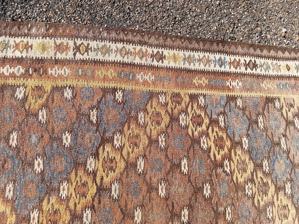 A long handwoven wool kilim runner rug with a repeating geometric diamond lattice pattern in terracotta brown and neutral tones. View IV