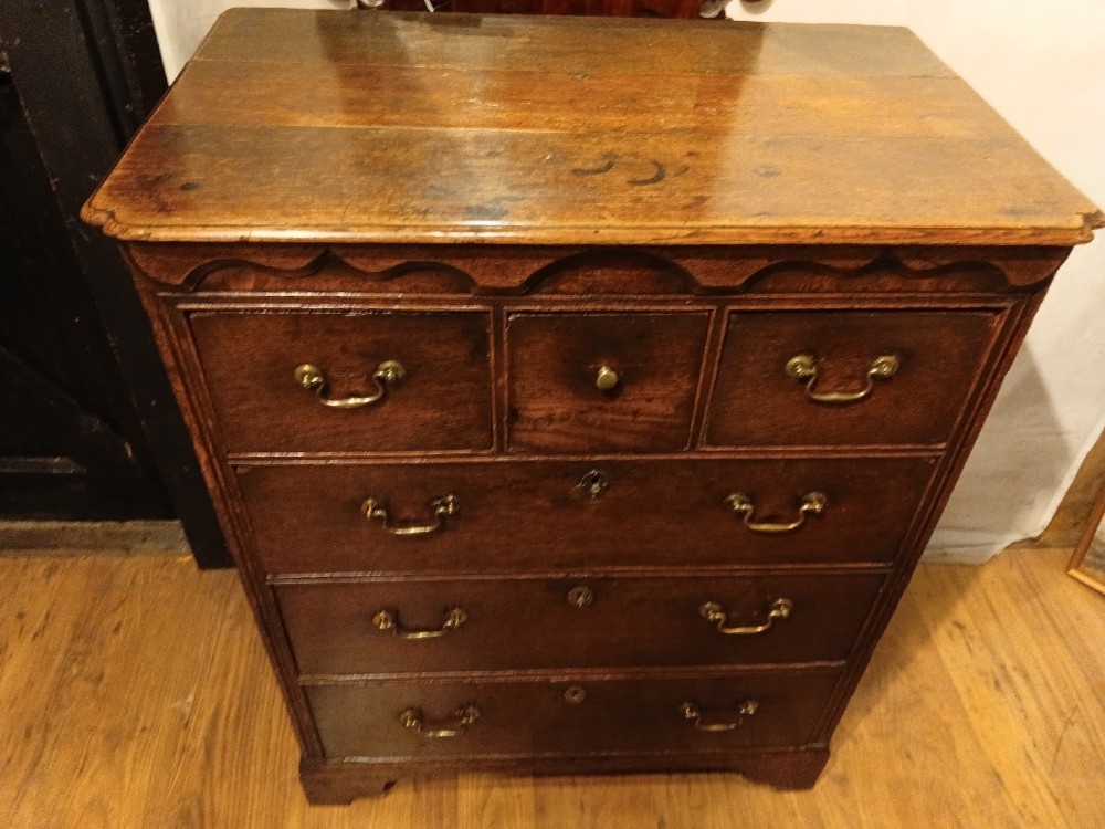 An antique brown oak chest of drawers featuring three small upper drawers over three long graduated drawers with brass drop handles.