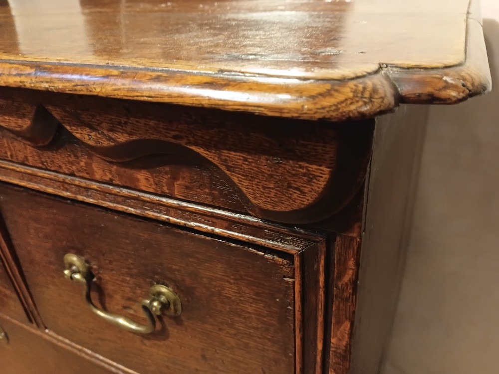 An antique brown oak chest of drawers featuring three small upper drawers over three long graduated drawers with brass drop handles. View III
