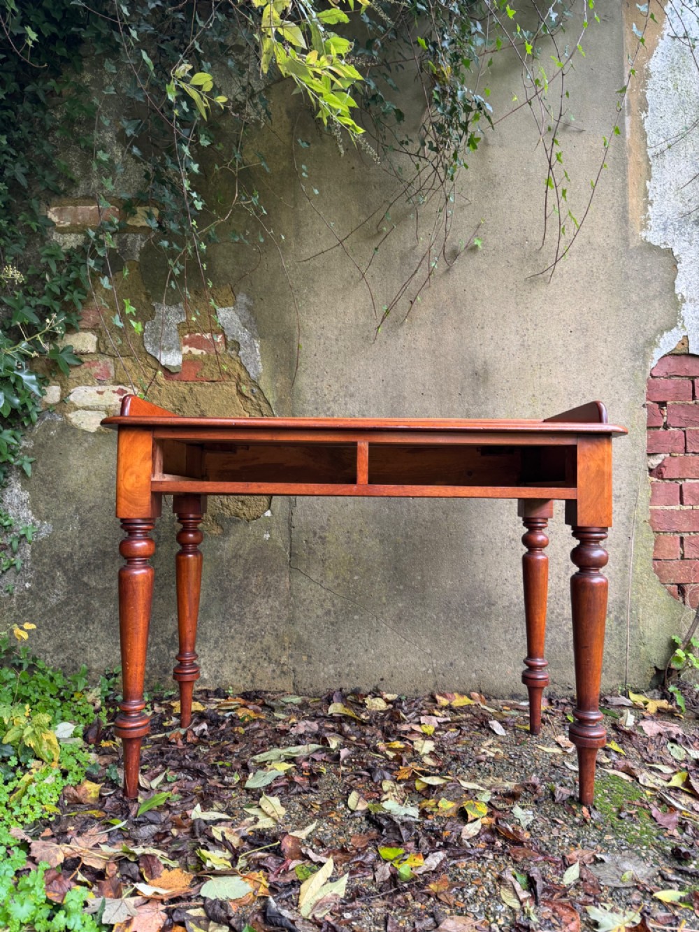 An antique reddish-brown mahogany writing table featuring two drawers with wooden knob handles, turned legs, and a three-sided raised rear gallery. View III