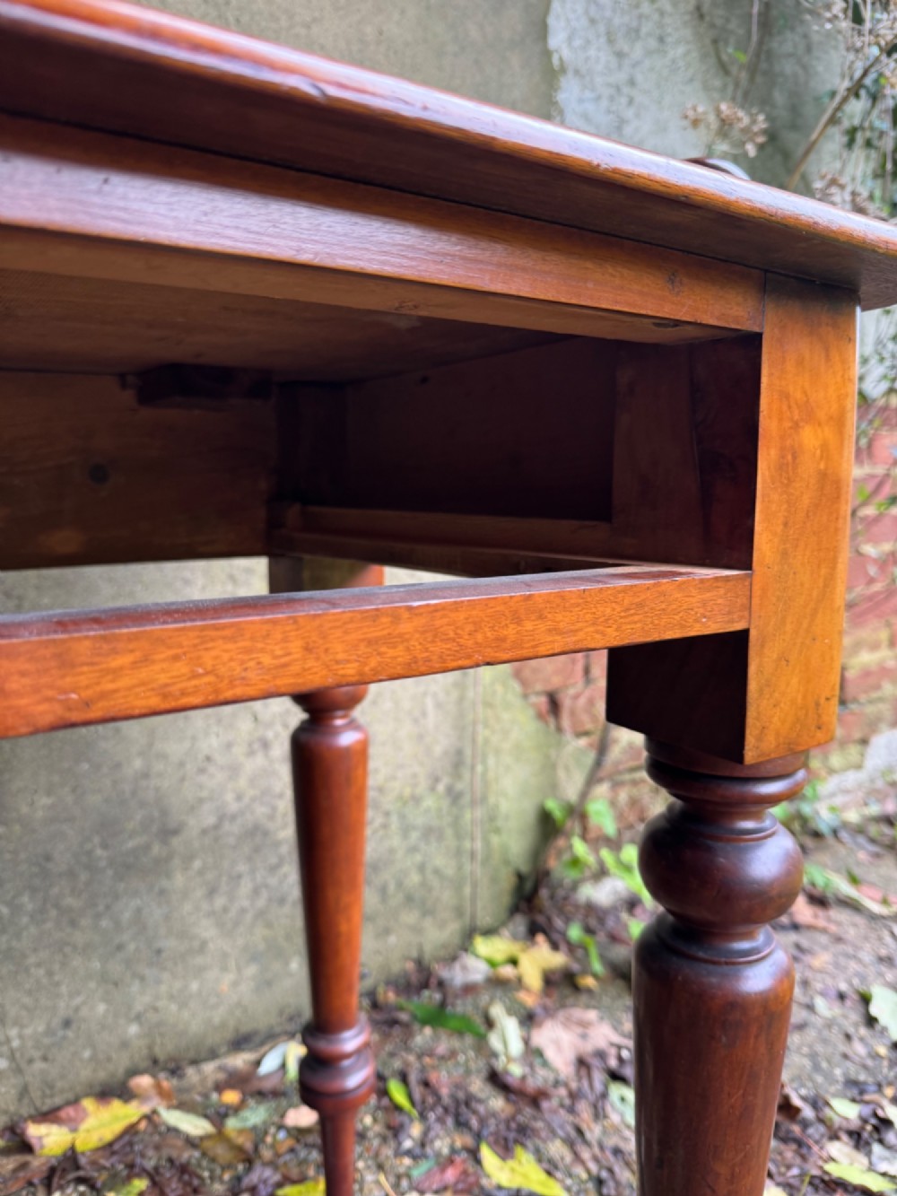 An antique reddish-brown mahogany writing table featuring two drawers with wooden knob handles, turned legs, and a three-sided raised rear gallery. View X