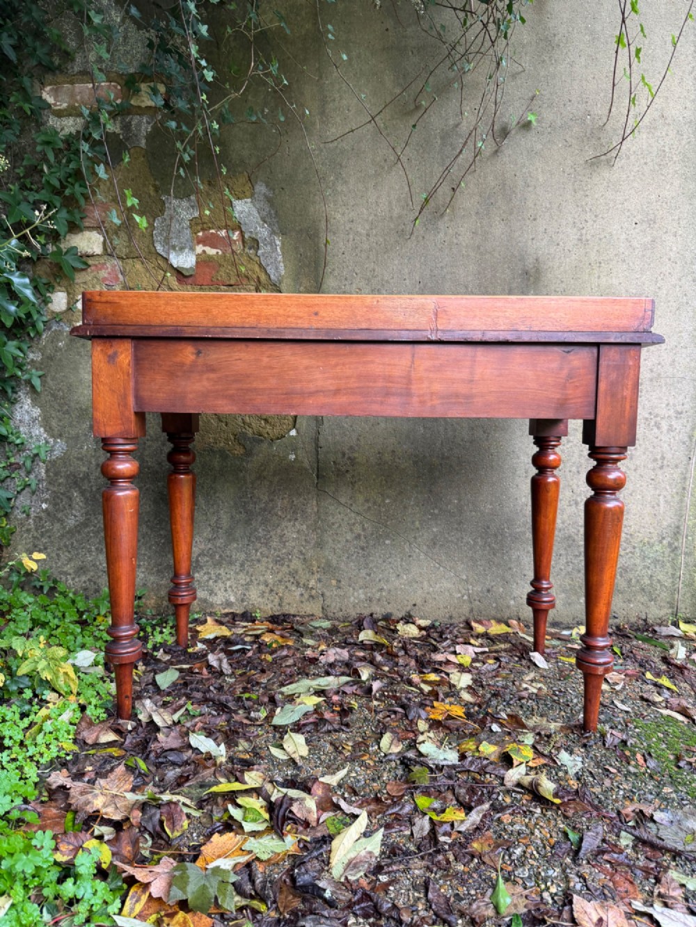 An antique reddish-brown mahogany writing table featuring two drawers with wooden knob handles, turned legs, and a three-sided raised rear gallery. View XII