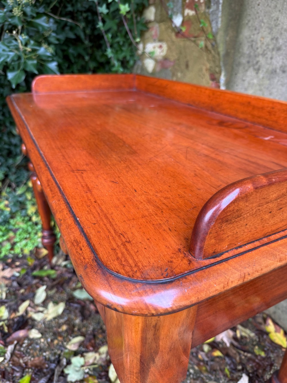 An antique reddish-brown mahogany writing table featuring two drawers with wooden knob handles, turned legs, and a three-sided raised rear gallery. View XIV