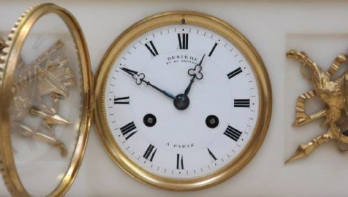 fig 1. An antique French Napoleon III mantel clock featuring a dark patinated bronze figure of Diana the Huntress holding a bow, set atop a rectangular white marble base with gilt-bronze mounts.