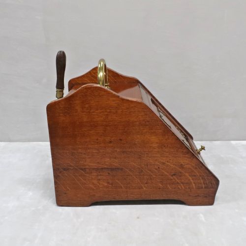 fig 2. A Victorian oak coal scuttle featuring a slanted drop-down front door decorated with brass corner mounts and a brass carrying handle on top.