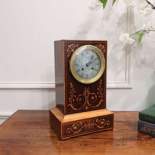 fig 1. A nineteenth-century rectangular dark rosewood mantel clock featuring foliate marquetry inlay, a brass-rimmed circular dial with Roman numerals, and a stepped plinth base.