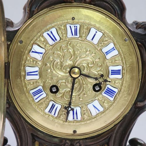 fig 2. A patinated dark bronze French Rococo style mantel clock featuring scrolling acanthus motifs, a floral finial, and blue Roman numerals on individual enamel cartouches.