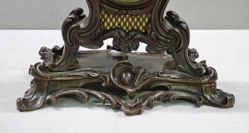 fig 3. A patinated dark bronze French Rococo style mantel clock featuring scrolling acanthus motifs, a floral finial, and blue Roman numerals on individual enamel cartouches.