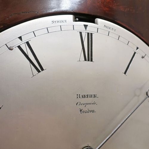 fig 3. A Georgian flame mahogany bracket clock featuring a circular white dial with Roman numerals, a pointed architectural pediment, and brass side frets.