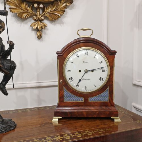 fig 1. A Regency mahogany bracket clock featuring brass mounts, a top handle, fishscale brass side frets, and a circular white dial signed Rives Bedford.
