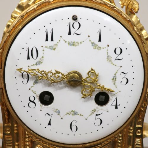 fig 2. An ornate French gilt bronze and white marble mantel clock featuring a white enamel dial topped with leaf motifs.