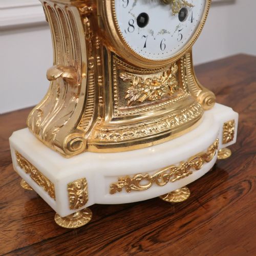 fig 3. An ornate French gilt bronze and white marble mantel clock featuring a white enamel dial topped with leaf motifs.