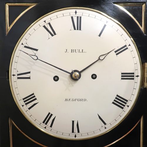 fig 2. An ebonised William IV bracket clock featuring brass inlays, a pineapple finial, lion mask side handles, ball feet, and a white circular dial with Roman numerals signed J. Bull Bedford.