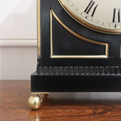 fig 5. An ebonised William IV bracket clock featuring brass inlays, a pineapple finial, lion mask side handles, ball feet, and a white circular dial with Roman numerals signed J. Bull Bedford.