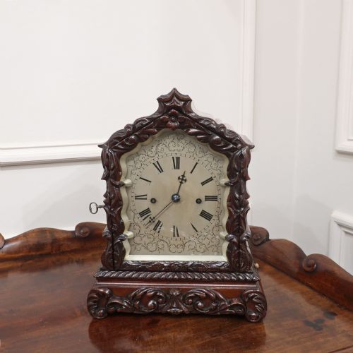 fig 1. An early Victorian mahogany library clock featuring a heavily carved leafy frame, Roman numeral dial face, and stepped side moulding.