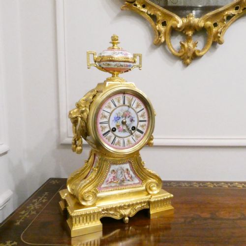 fig 1. A French Louis XV style gilt bronze mantel clock featuring a hand-painted porcelain dial, lower cherub panel, scroll feet, and an ornamental urn finial.