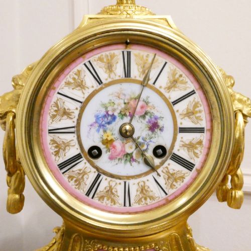 fig 2. A French Louis XV style gilt bronze mantel clock featuring a hand-painted porcelain dial, lower cherub panel, scroll feet, and an ornamental urn finial.