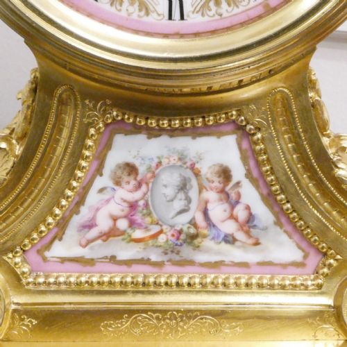 fig 4. A French Louis XV style gilt bronze mantel clock featuring a hand-painted porcelain dial, lower cherub panel, scroll feet, and an ornamental urn finial.