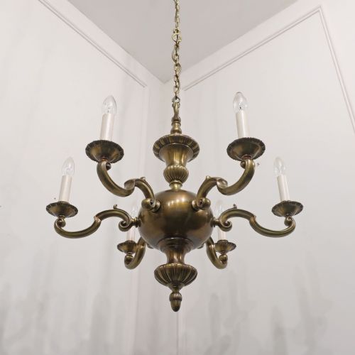 fig 2. An Edwardian brass six-arm chandelier hanging from a link chain, featuring curved S-scroll branches and candle-style bulb holders.