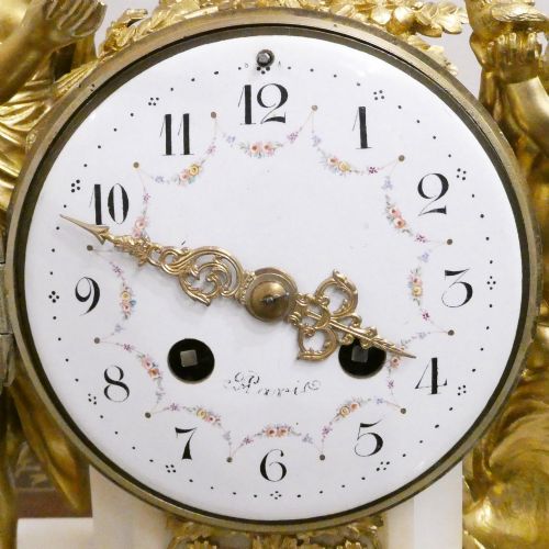 fig 1. A French Louis XVI style gilt bronze and white marble mantel clock featuring classical female and winged cherub figures surrounding a white enamel dial.