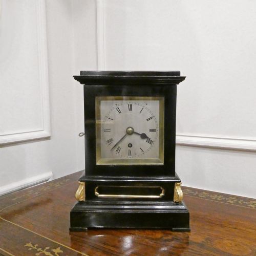 fig 1. An early Victorian ebonised wooden library clock featuring a square dial with Roman numerals, side viewing apertures, and brass accents.