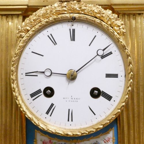 fig 2. A French Louis XVI style gilt bronze mantel clock featuring a top urn finial, fluted side columns, and hand-painted blue porcelain panels around a white enamel dial.