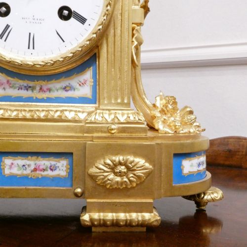 fig 3. A French Louis XVI style gilt bronze mantel clock featuring a top urn finial, fluted side columns, and hand-painted blue porcelain panels around a white enamel dial.