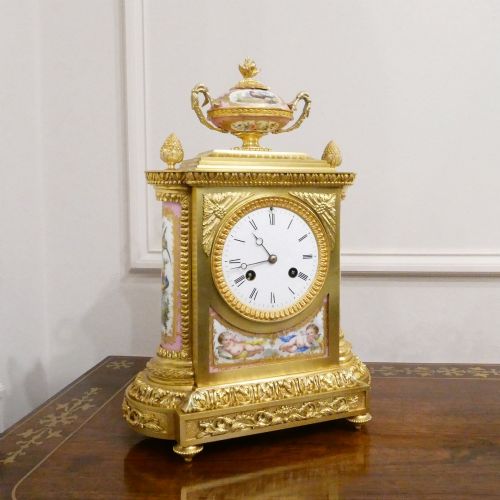 fig 1. An antique French gilt bronze mantel clock featuring hand-painted pink porcelain panels, a porcelain urn finial, and an enamel dial with Roman numerals.
