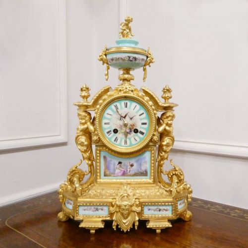 fig 1. A French 19th-century gilt bronze mantel clock featuring light blue hand-painted porcelain panels, sculpted putti, an urn finial, and an enamel Roman numeral dial.