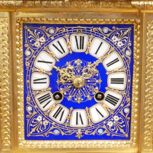 fig 1. A French gilt bronze mantel clock featuring two cherub figures atop an ornate golden structure with cobalt blue porcelain panels and Roman numerals.
