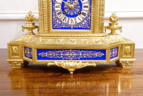 fig 3. A French gilt bronze mantel clock featuring two cherub figures atop an ornate golden structure with cobalt blue porcelain panels and Roman numerals.