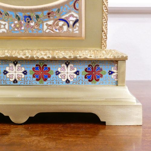 fig 3. A nineteenth-century French gilt brass mantel clock featuring colourful champleve enamel geometric patterns, flanked by two matching decorative urns.
