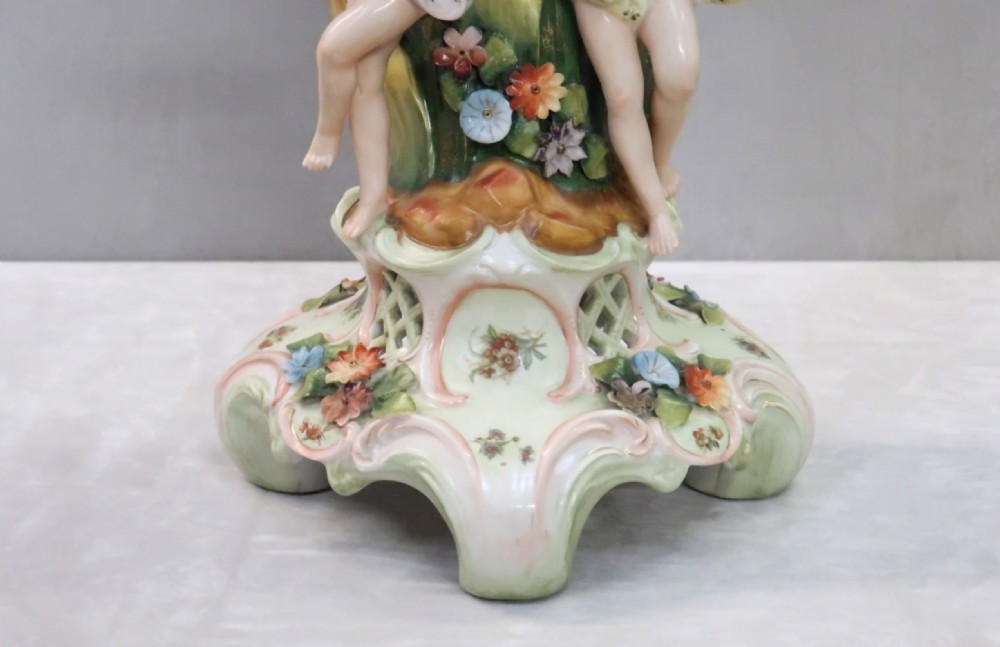 A polychrome Saxony porcelain fruit centrepiece featuring a reticulated floral-encrusted basket supported by two cherub figures on a scrolled base. View V