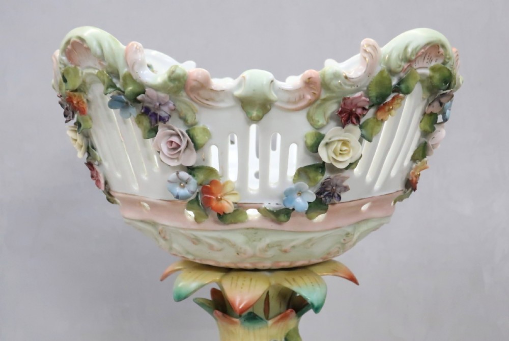 A polychrome Saxony porcelain fruit centrepiece featuring a reticulated floral-encrusted basket supported by two cherub figures on a scrolled base. View VII
