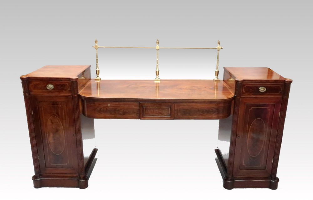 A Georgian mahogany pedestal sideboard featuring twin end pedestals with oval inlaid cupboards, a central frieze drawer, and a brass gallery along the back rail.