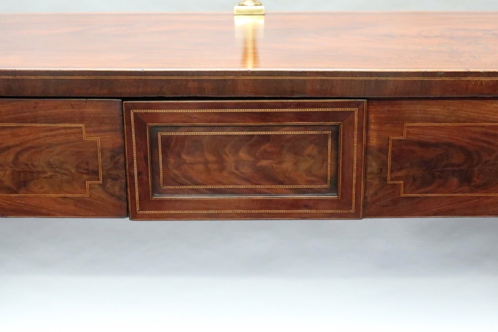 A Georgian mahogany pedestal sideboard featuring twin end pedestals with oval inlaid cupboards, a central frieze drawer, and a brass gallery along the back rail. View V