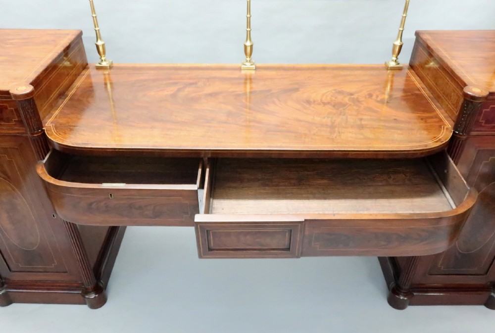 A Georgian mahogany pedestal sideboard featuring twin end pedestals with oval inlaid cupboards, a central frieze drawer, and a brass gallery along the back rail. View XII