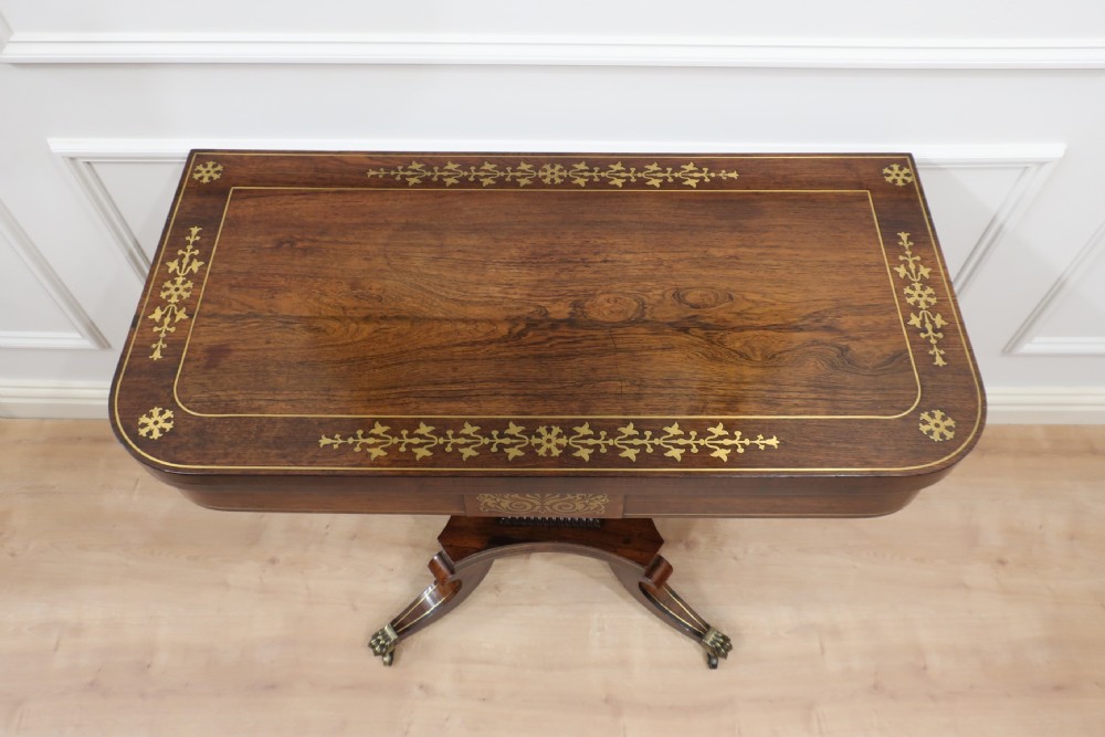 A Regency dark rosewood fold-over table featuring floral brass inlay motifs and a central pedestal supported by four splayed legs with brass lion paw feet. View II