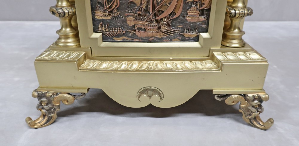 A French 19th-century gilt brass mantel clock featuring relief panels, flanked by two matching ornamental urn garnitures on detailed bases. View VII
