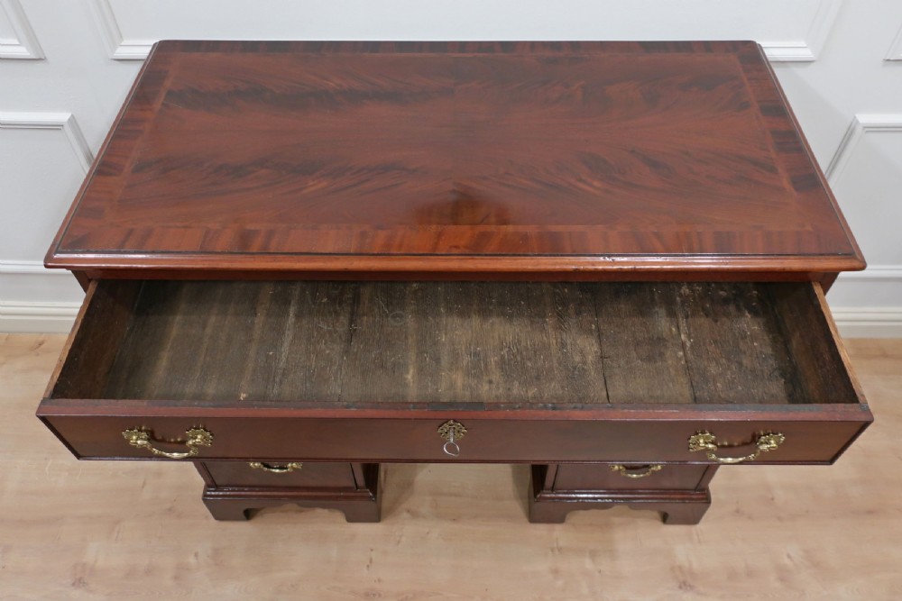 An antique dark mahogany Georgian kneehole desk featuring a central carved cupboard flanked by drawers with ornate brass handles. View II
